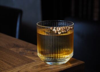 Segelas minuman beralkohol di atas meja kayu, ilustrasi hukum khamr dalam Islam
