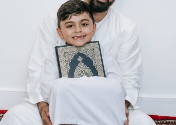 Ayah dan anak tersenyum memegang mushaf Al-Qur'an, ilustrasi hadits 3 amal yang tidak terputus pahalanya