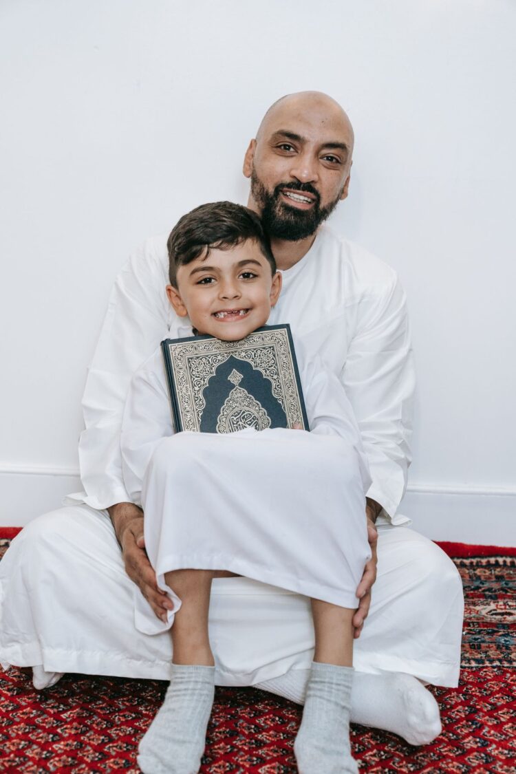 Ayah dan anak tersenyum memegang mushaf Al-Qur'an, ilustrasi hadits 3 amal yang tidak terputus pahalanya