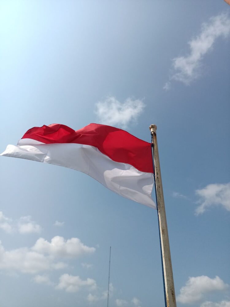 Bendera merah putih Indonesia berkibar di langit biru, ilustrasi klarifikasi hadits hubbul wathan minal iman