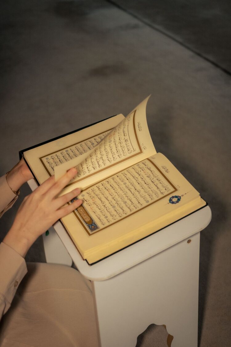 Tangan membuka lembaran mushaf Al-Qur'an, ilustrasi hadits tentang keutamaan membaca Al-Qur'an