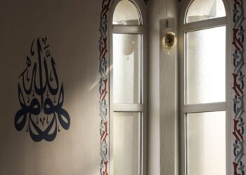 Interior masjid dengan kaligrafi Arab dan cahaya matahari dari jendela lengkung, ilustrasi hukum merayakan Maulid Nabi