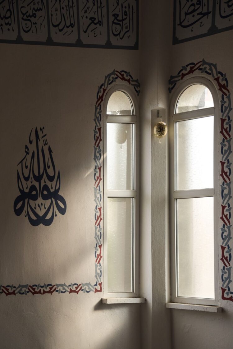 Interior masjid dengan kaligrafi Arab dan cahaya matahari dari jendela lengkung, ilustrasi hukum merayakan Maulid Nabi