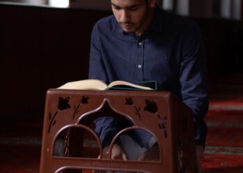 Seorang pemuda membaca Al-Qur'an di dalam masjid, ilustrasi hadits tentang pemuda yang tumbuh dalam ibadah