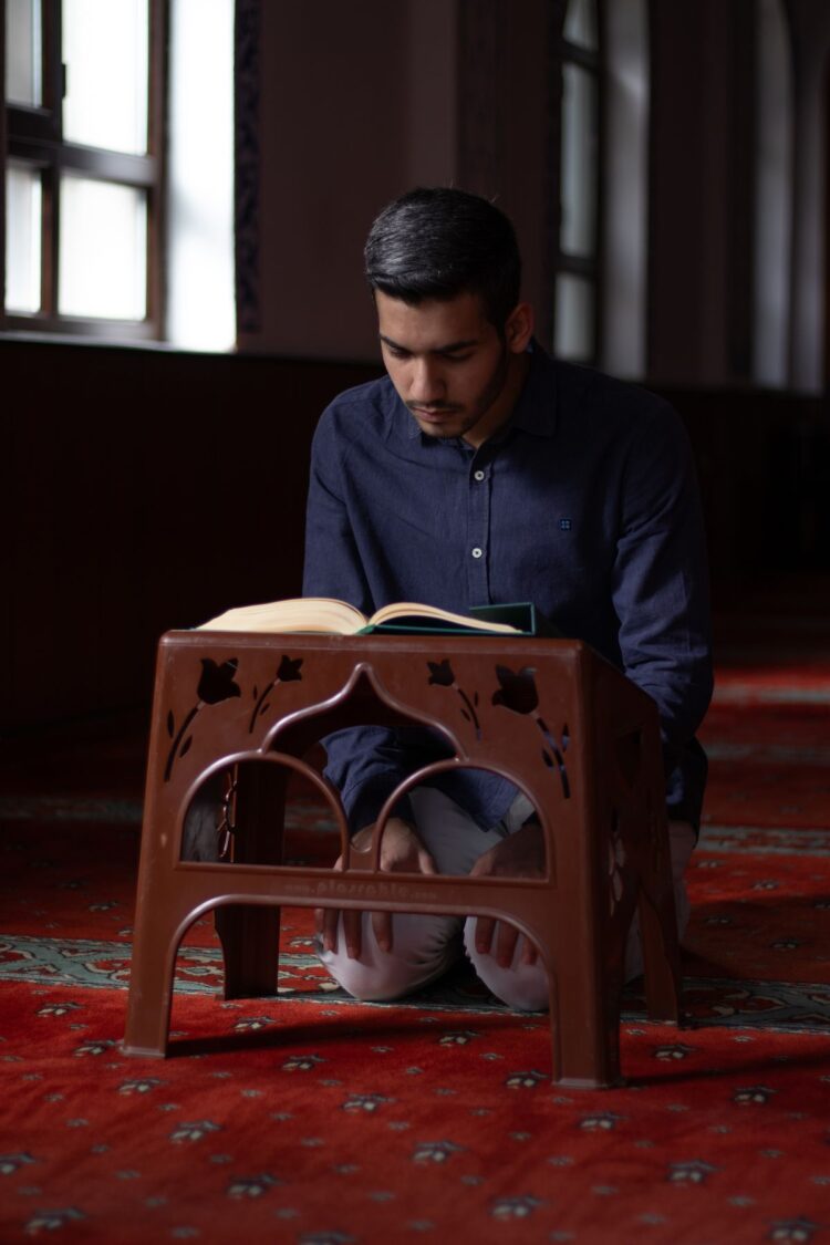Seorang pemuda membaca Al-Qur'an di dalam masjid, ilustrasi hadits tentang pemuda yang tumbuh dalam ibadah