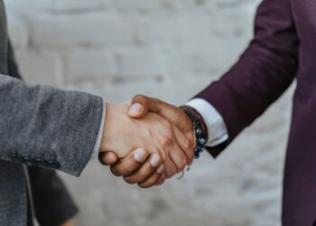Dua orang berjabat tangan menutup kesepakatan bisnis, ilustrasi klarifikasi hadits 9 dari 10 pintu rezeki di perdagangan
