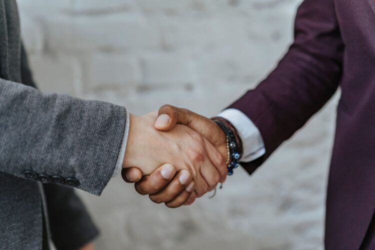 Dua orang berjabat tangan menutup kesepakatan bisnis, ilustrasi klarifikasi hadits 9 dari 10 pintu rezeki di perdagangan