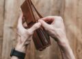 Tangan membuka dompet kulit berisi uang, ilustrasi barang temuan