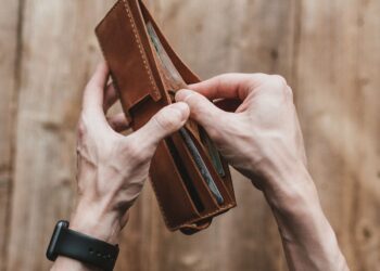 Tangan membuka dompet kulit berisi uang, ilustrasi barang temuan
