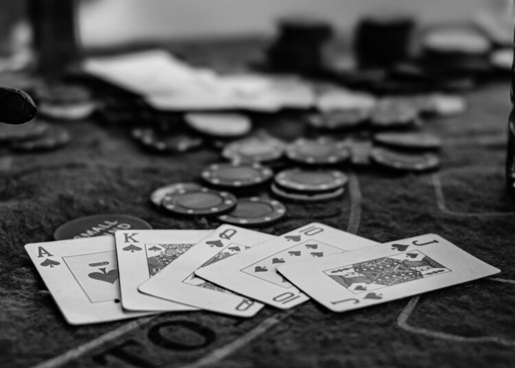 Kartu remi dan chip poker di atas meja kasino, foto hitam putih