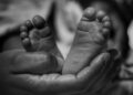 Kaki bayi mungil digenggam lembut oleh tangan orang dewasa