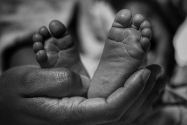 Kaki bayi mungil digenggam lembut oleh tangan orang dewasa