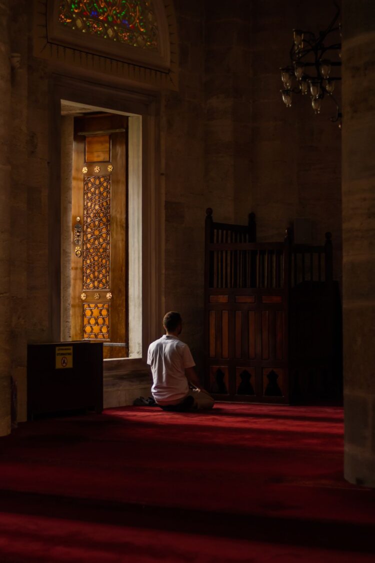 Seorang pria duduk sendirian beribadah di dalam masjid, ilustrasi hukum i'tikaf dalam Islam