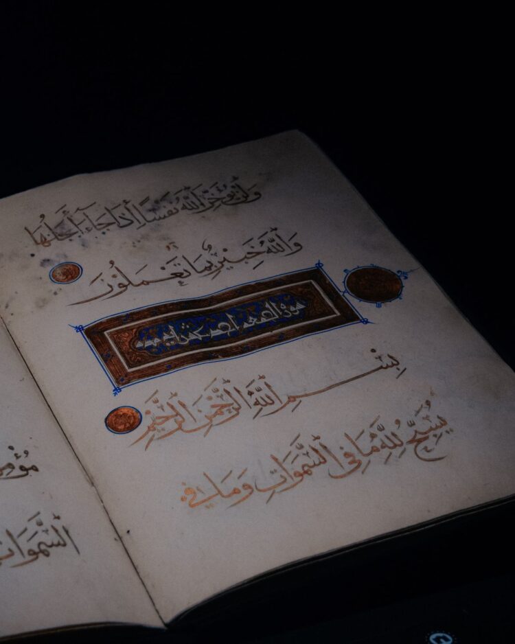 Mushaf Al-Qur'an kuno terbuka dengan kaligrafi berhiaskan emas di latar gelap, ilustrasi keutamaan 2 ayat terakhir Surat Al-Baqarah