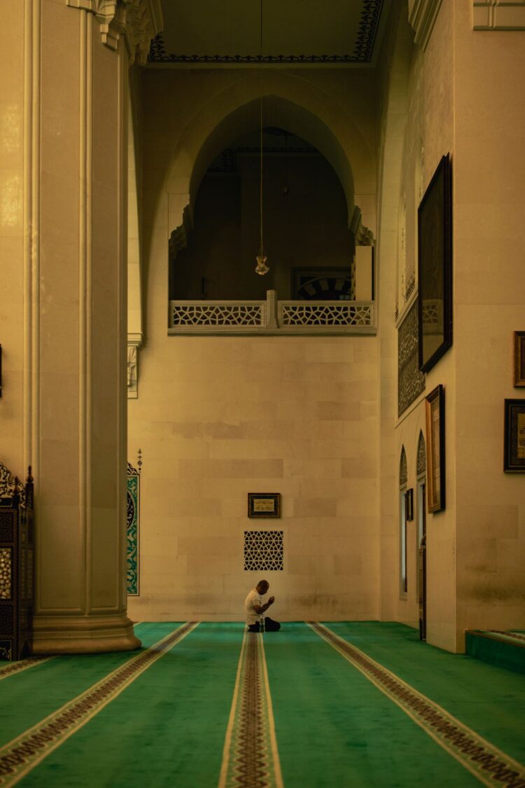 Seorang pria shalat sendirian di dalam masjid besar, ilustrasi keutamaan Surat Al-Fatihah sebagai induk Al-Qur'an