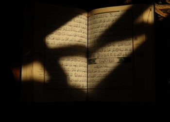 Mushaf Al-Qur'an terbuka menunjukkan awal Surat Al-Kahfi disinari cahaya matahari, ilustrasi keutamaan membaca Al-Kahfi di hari Jumat