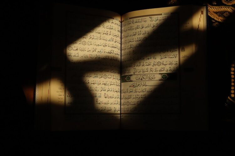 Mushaf Al-Qur'an terbuka menunjukkan awal Surat Al-Kahfi disinari cahaya matahari, ilustrasi keutamaan membaca Al-Kahfi di hari Jumat