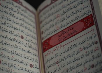 Tangan memegang mushaf Al-Qur'an terbuka, ilustrasi keutamaan membaca Surat Al-Waqiah