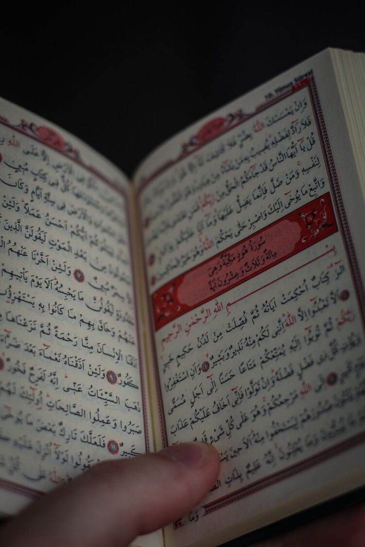Tangan memegang mushaf Al-Qur'an terbuka, ilustrasi keutamaan membaca Surat Al-Waqiah