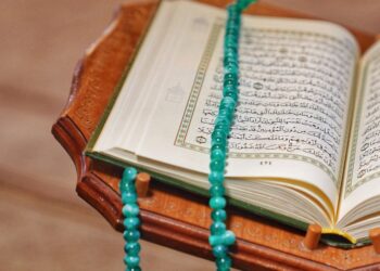 Mushaf Al-Qur'an terbuka dengan tasbih hijau di atasnya, ilustrasi keutamaan dzikir pagi dan petang