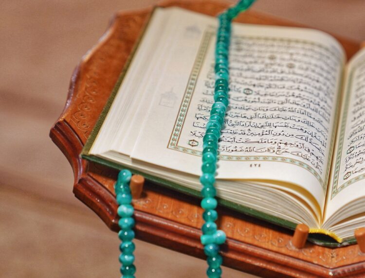 Mushaf Al-Qur'an terbuka dengan tasbih hijau di atasnya, ilustrasi keutamaan dzikir pagi dan petang