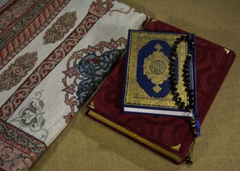 Mushaf Al-Qur'an bersampul biru emas dengan tasbih hitam di atas sajadah, ilustrasi keutamaan dzikir tasbih subhanallah