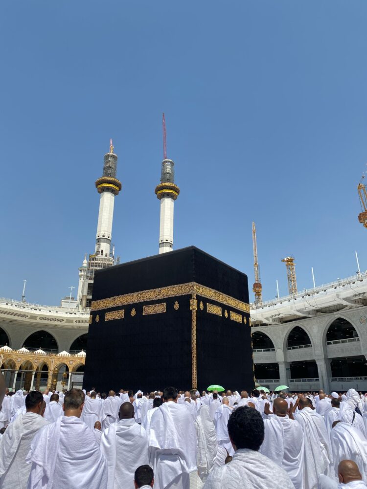 Jamaah haji berpakaian ihram putih menghadap Ka'bah di siang hari, ilustrasi keutamaan haji mabrur