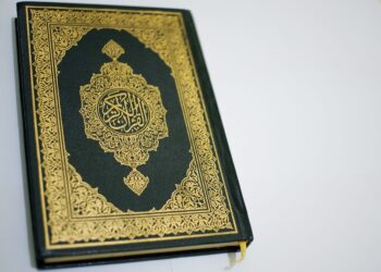 Mushaf Al-Qur'an tertutup dengan sampul hijau berhias kaligrafi emas, ilustrasi keutamaan khatam Al-Qur'an