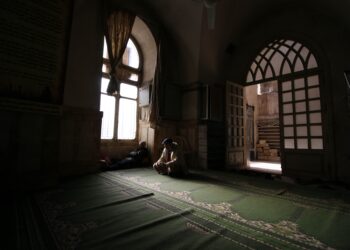 Dua orang duduk tenang di dalam masjid dengan cahaya dari jendela, ilustrasi keutamaan menghadiri majelis ilmu