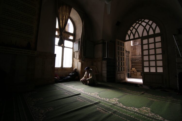 Dua orang duduk tenang di dalam masjid dengan cahaya dari jendela, ilustrasi keutamaan menghadiri majelis ilmu