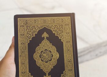 Tangan memegang mushaf Al-Qur'an bersampul hitam emas, ilustrasi keutamaan Nuzulul Qur'an