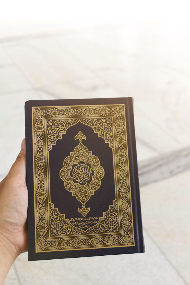 Tangan memegang mushaf Al-Qur'an bersampul hitam emas, ilustrasi keutamaan Nuzulul Qur'an