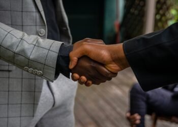 Dua orang berjabat tangan mengenakan jas formal, ilustrasi keutamaan sifat pemaaf dalam Islam