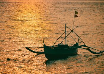 Perahu tradisional dengan siluet saat matahari terbenam di laut, ilustrasi keutamaan sholawat munjiyat dan bershalawat kepada Nabi