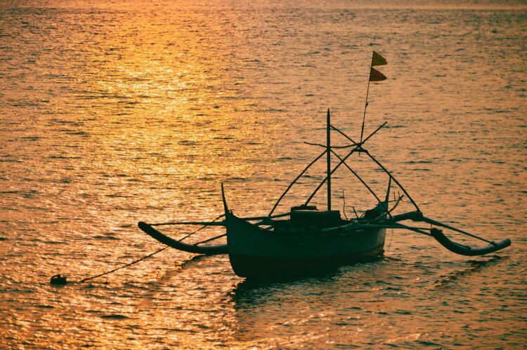 Perahu tradisional dengan siluet saat matahari terbenam di laut, ilustrasi keutamaan sholawat munjiyat dan bershalawat kepada Nabi