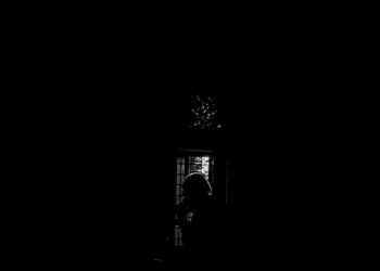Siluet seseorang shalat di dalam masjid yang gelap, ilustrasi keutamaan shalat witir sebagai penutup ibadah malam