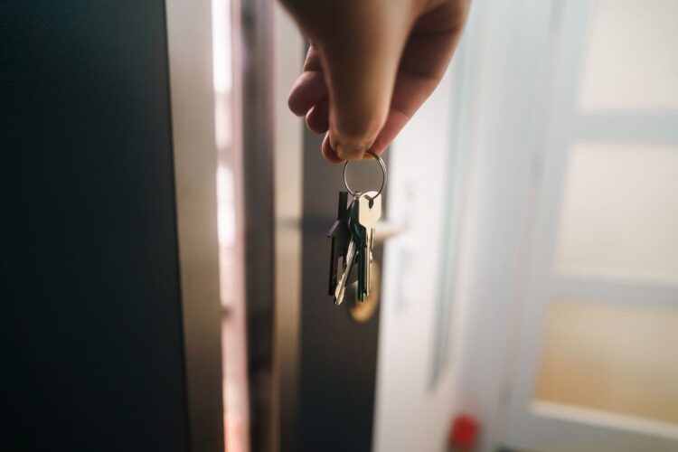 Tangan memegang kunci di depan pintu apartemen, ilustrasi hukum kumpul kebo dalam Islam