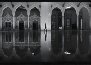 Siluet seseorang berjalan di lorong masjid, ilustrasi hukum lewat di depan orang yang sedang shalat