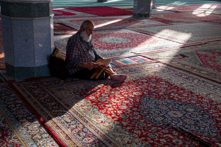 Seorang pria membaca Al-Qur'an di masjid, ilustrasi hukum ruqyah dalam Islam