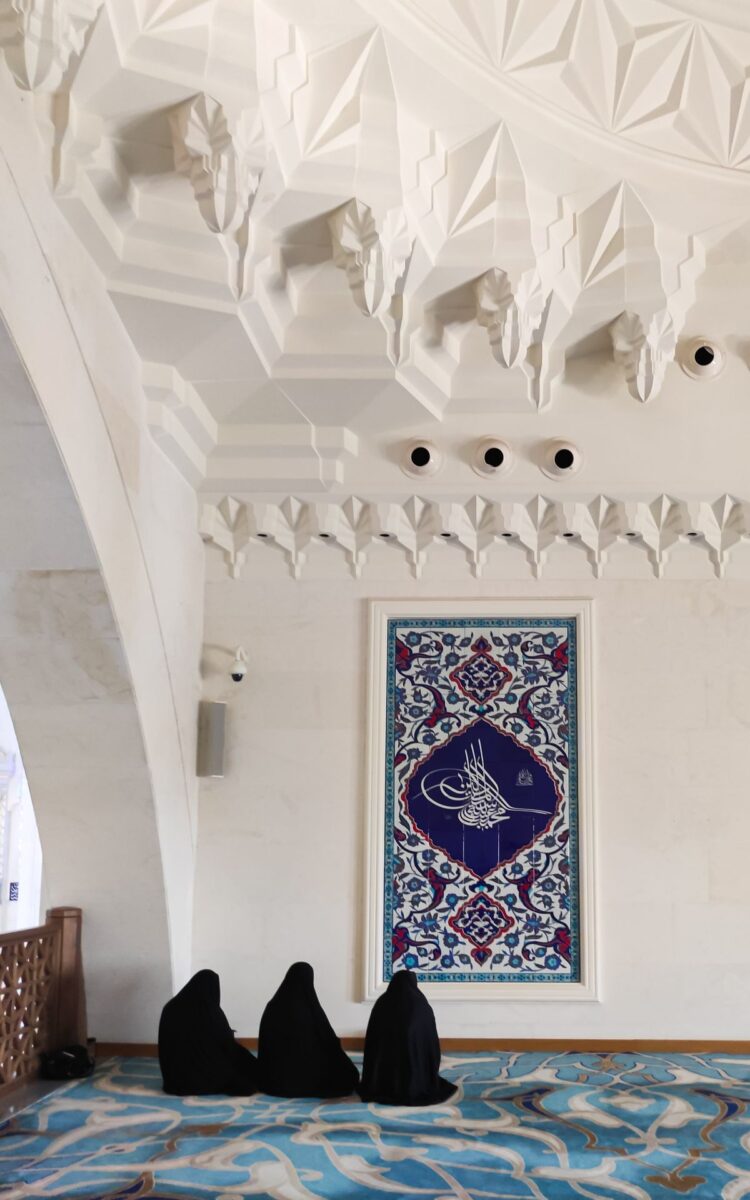Tiga wanita berjilbab hitam duduk shalat di masjid, ilustrasi hukum wanita ikut shalat Jumat