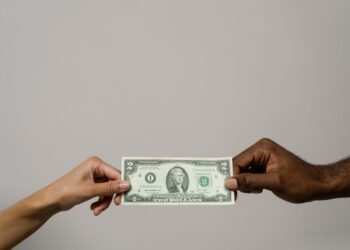 Tangan menyerahkan uang kertas ke tangan lain, ilustrasi perbedaan zakat, infaq, sedekah dan wakaf